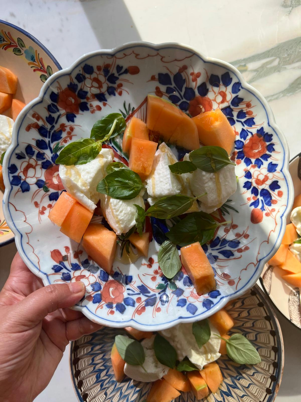 Hand holding a painted plate of melon, mozzarella and fresh basil