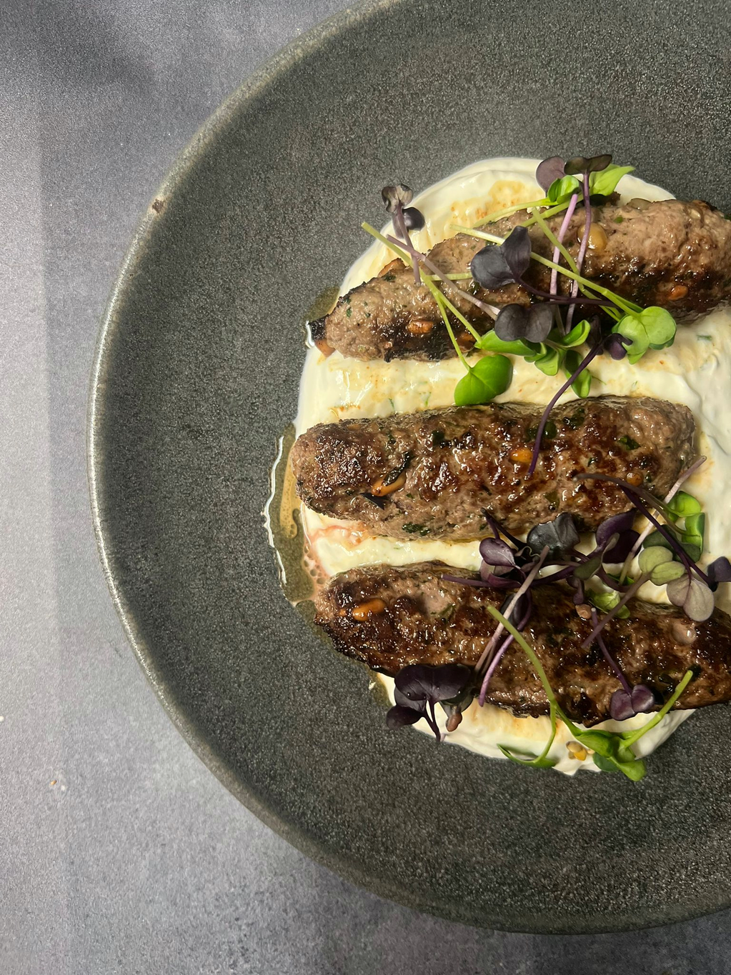 Grilled kofta on whipped labneh with microgreens in a stone bowl