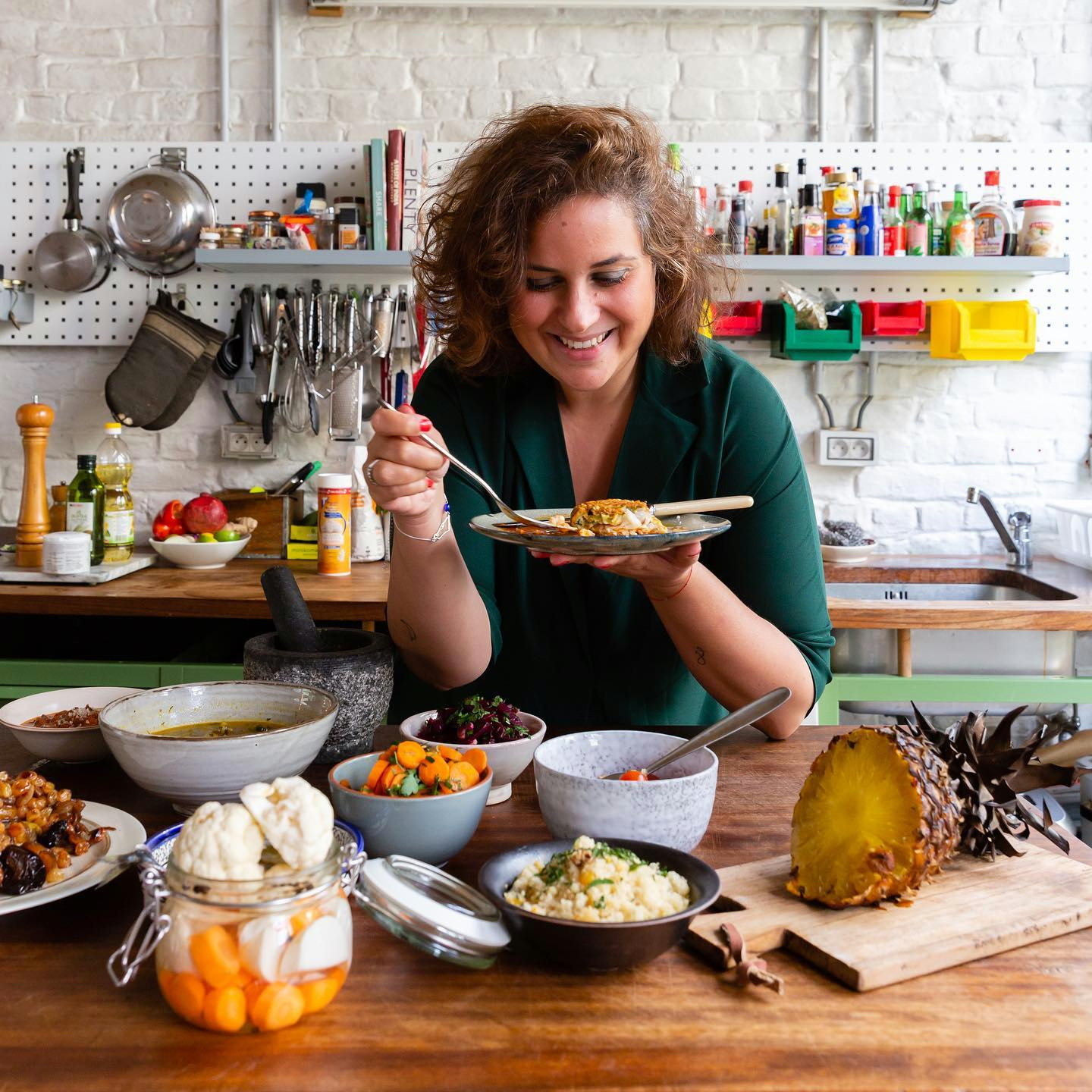 Chef Simona El-Harar tasting a dish behind a table of Mediterranean plates in her kitchen